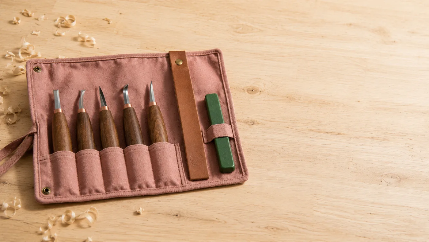 The canvas tool roll opened flat on a workbench, the five walnut-handled carving knives seated in their pockets beside the leather strop