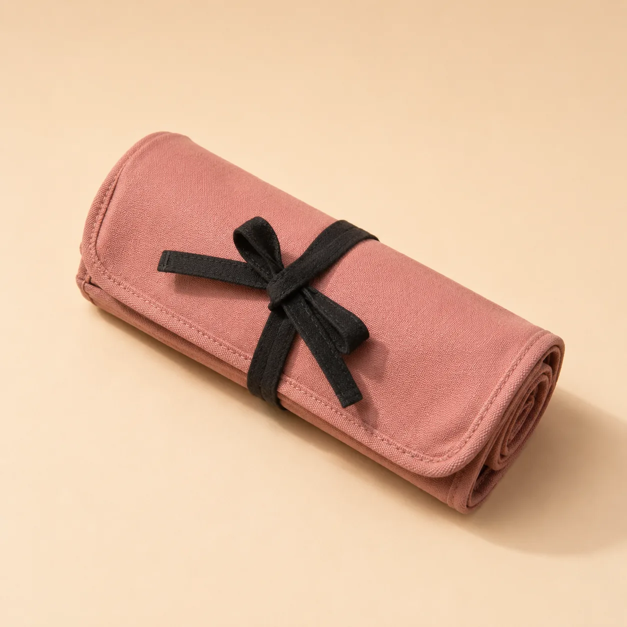 The tool roll closed and tied with its black cotton strap, photographed against a plain warm background
