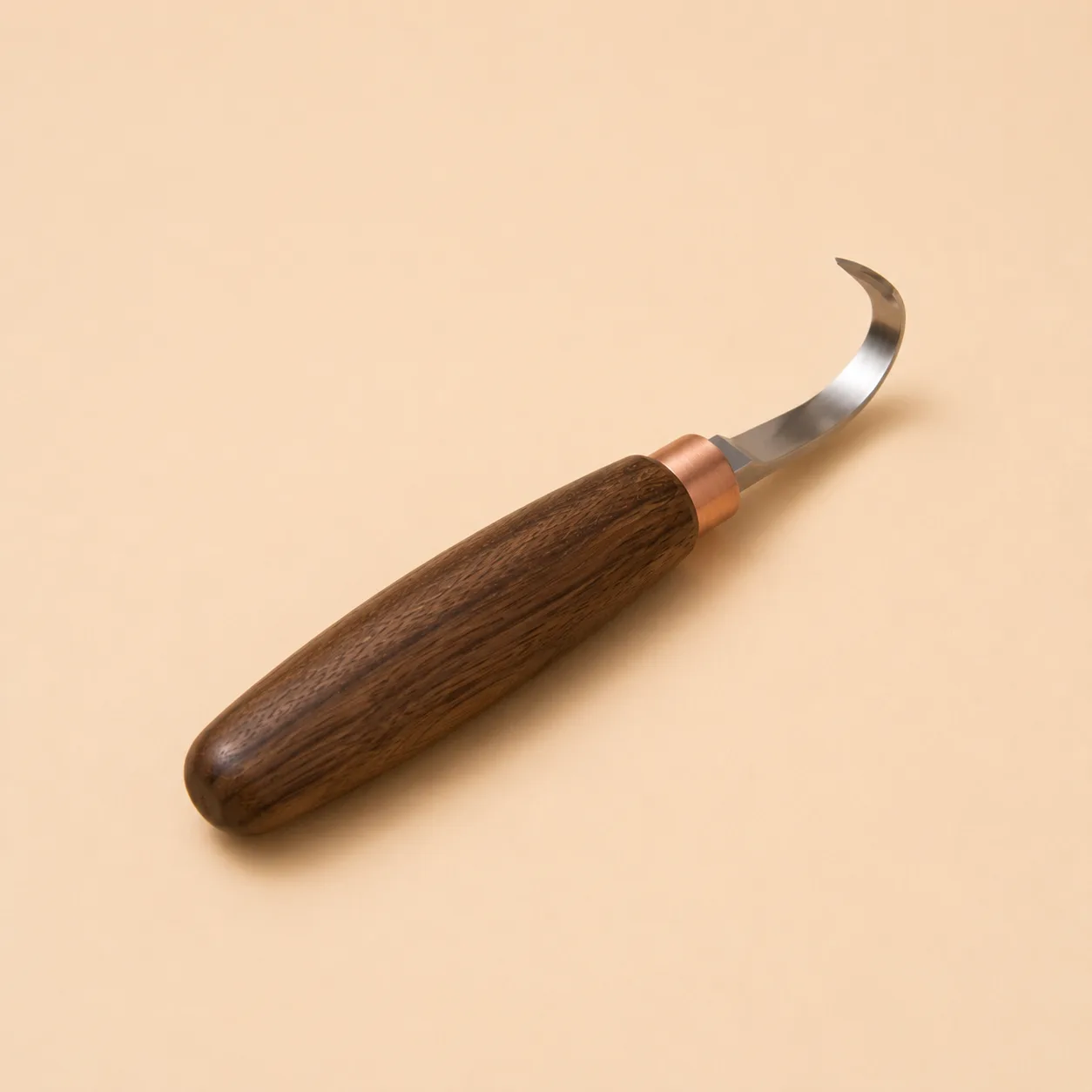 The hook knife photographed alone against a warm plain background, its curved steel blade and walnut handle in full view