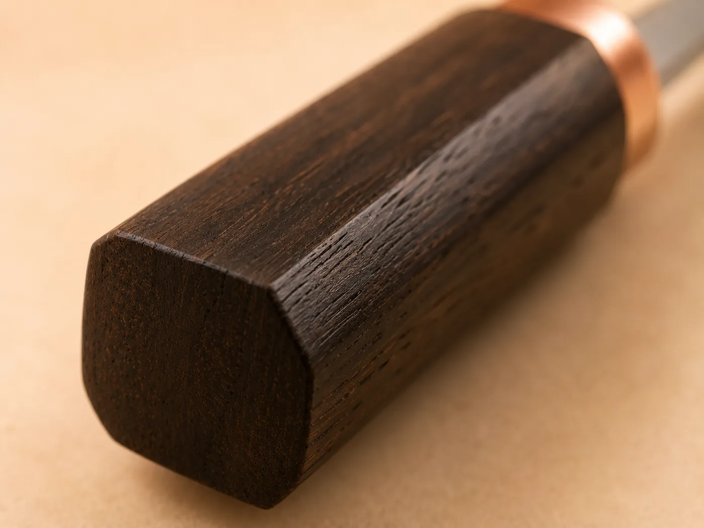 Extreme close-up of a black walnut knife handle, its dark grain and square faceted profile filling the frame