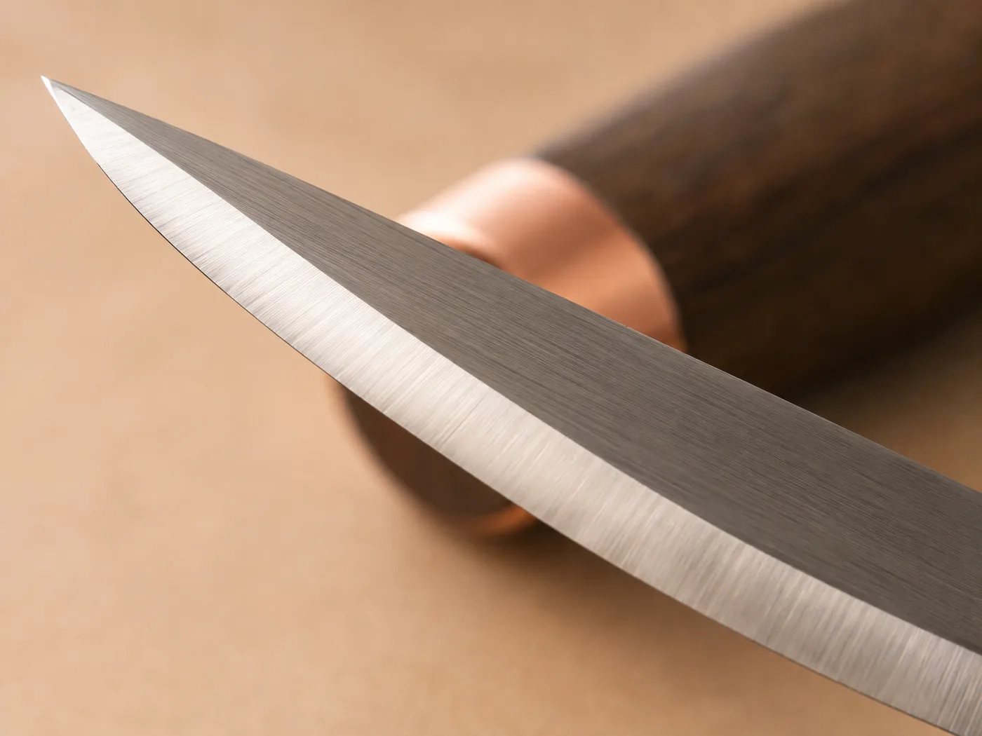 Extreme close-up of a polished carving blade edge catching the light, the dark walnut handle blurred behind it