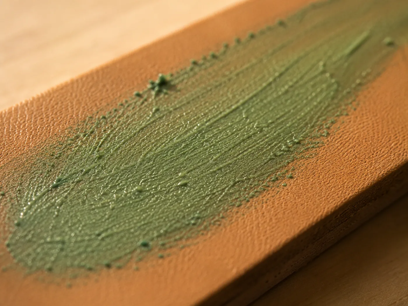 Extreme close-up of green polishing compound smeared across the grain of tan leather