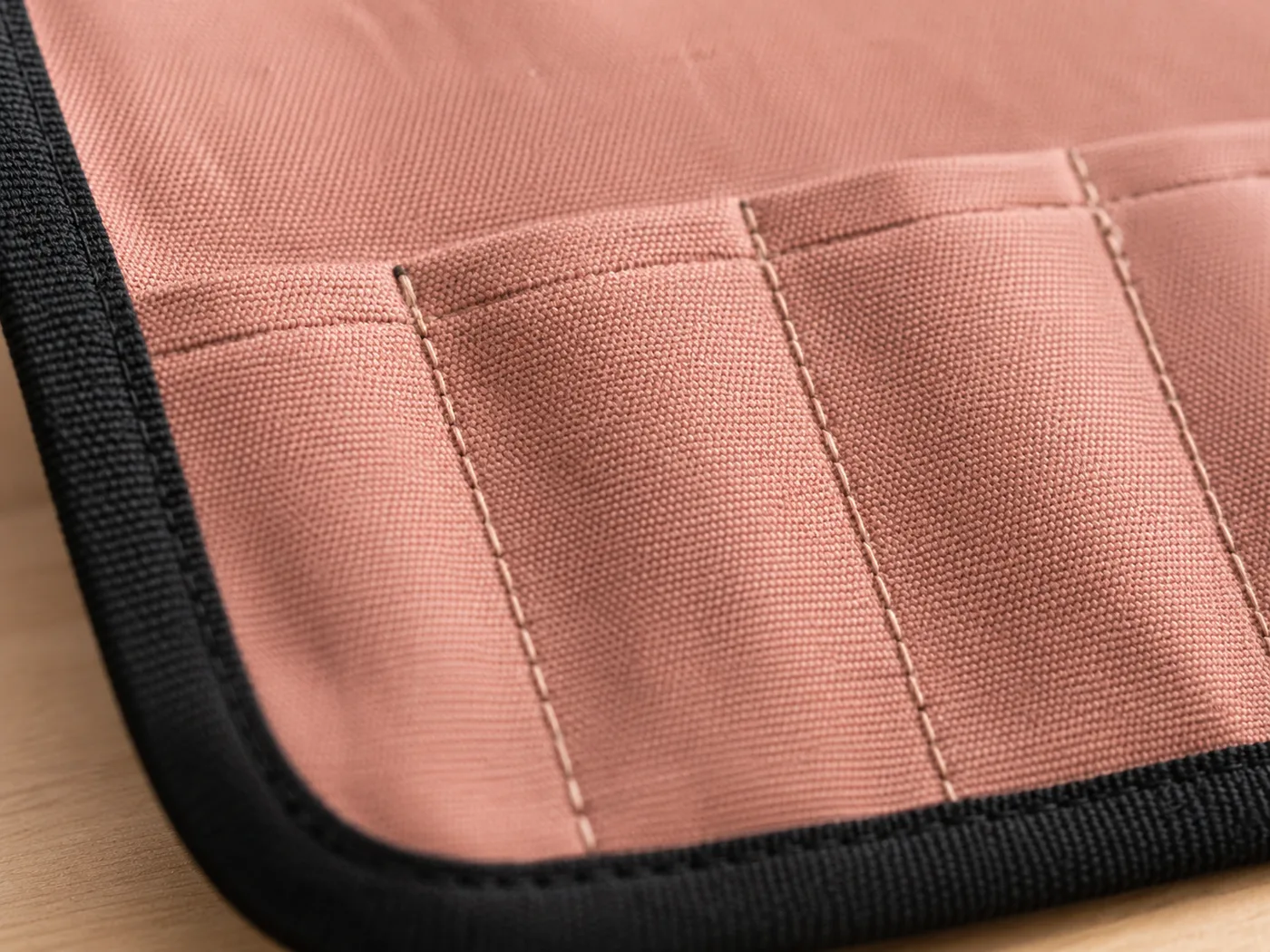 Extreme close-up of the canvas roll fabric, its black bound edge and the stitching of the knife pockets